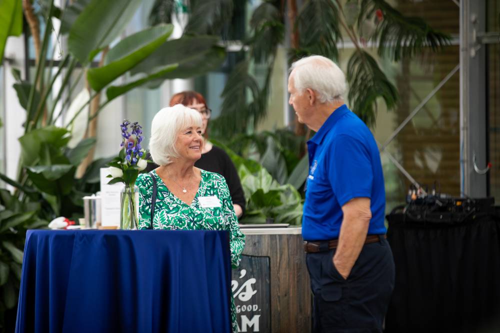 Deb Barko standing by table at event, chatting with male coworker